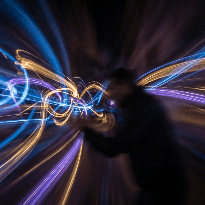 Swirling trails of blue, purple, and gold light against a dark, blurred backdrop.