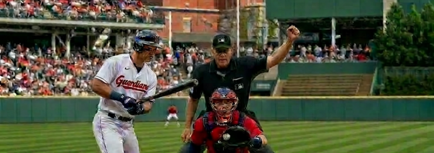 Pitcher throwing ball towards batter while catcher and umpire prepare at home plate in Cleveland stadium